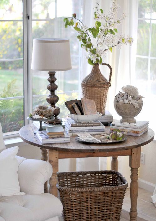 mesa con una lampara, varios libros, jarrones, plantas